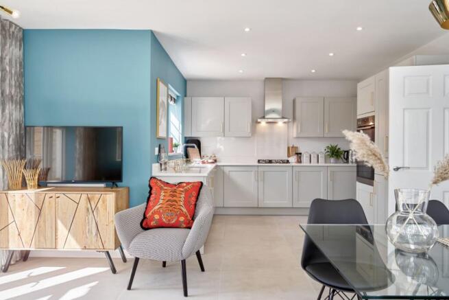A modern living and kitchen area features a grey armchair with a patterned cushion in the foreground