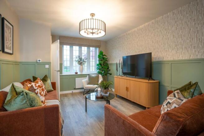 Two orange sofas with green and patterned pillows face a coffee table and a TV on a wooden cabinet