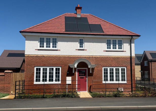 A modern two-story house with a red-tiled roof and solar panels sits behind a black metal fence